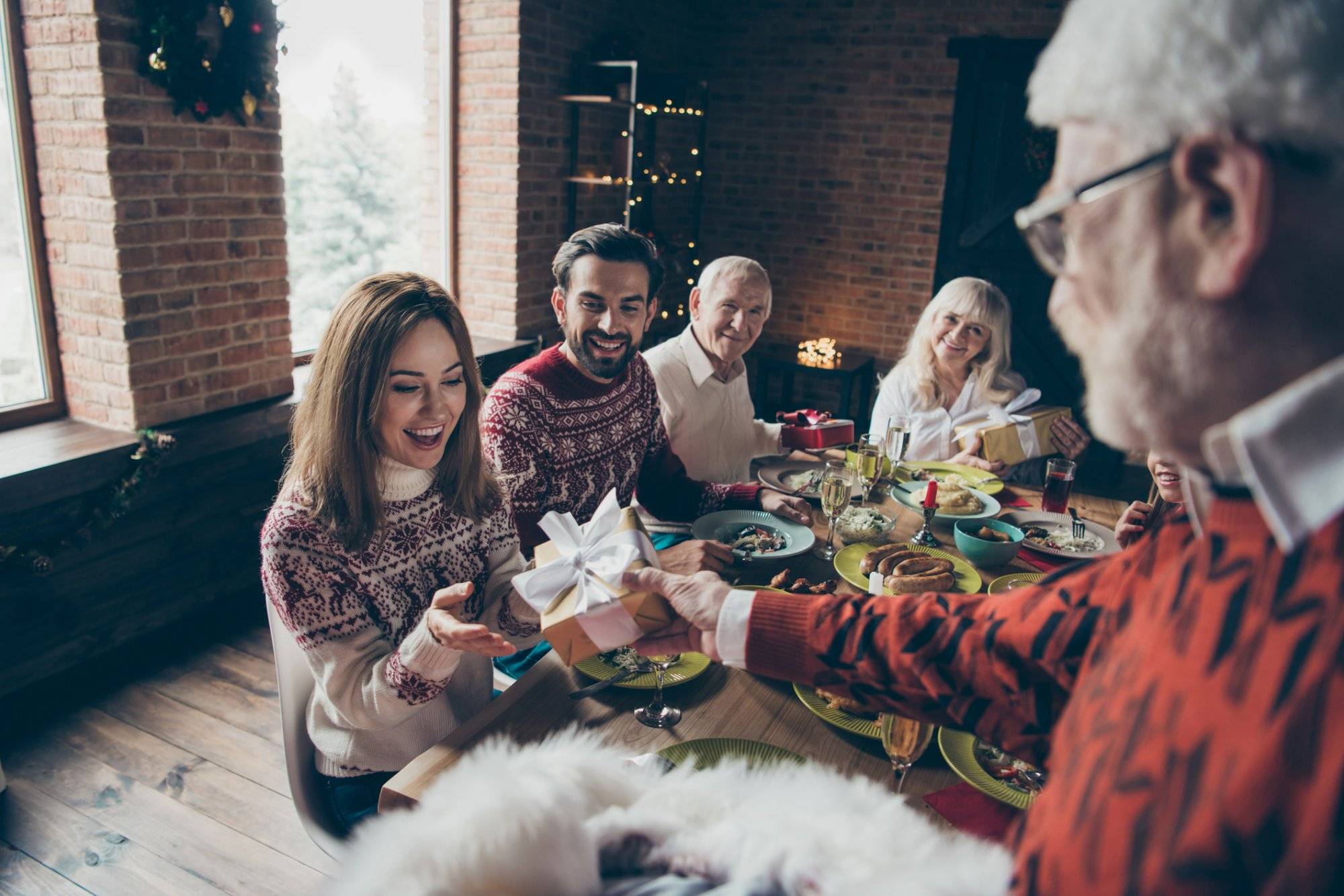 Noel morning family gathering. Nice adorable cheerful grey-haired grandparents, relatives, pre-teen sister, brother at house feast, sitting at lunch table, getting surprise presents fun joy